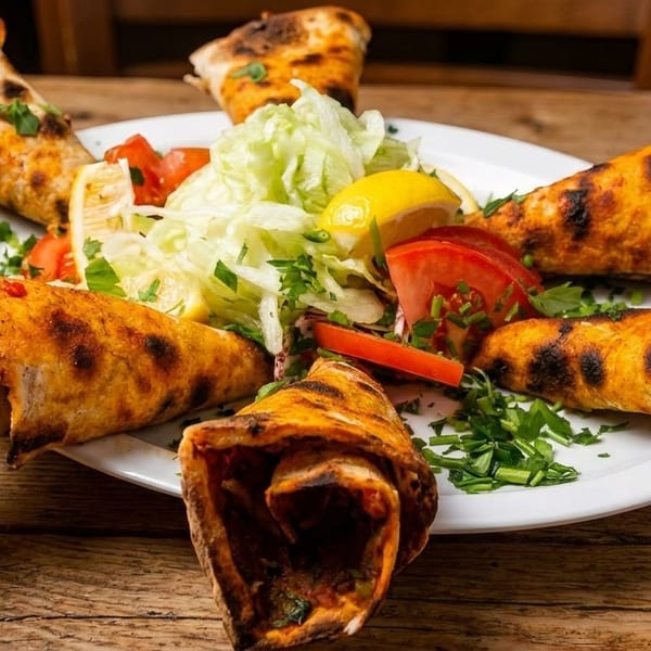 Six grilled wraps with meat filling, served with a fresh salad of lettuce, tomatoes, and lemon.