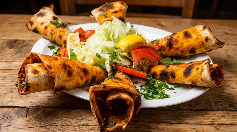 Six grilled wraps with meat filling, served with a fresh salad of lettuce, tomatoes, and lemon.
