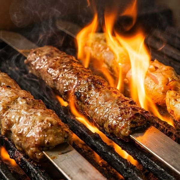 Three skewers of meat, two ground and one chicken, grilling over open flames on a barbecue.