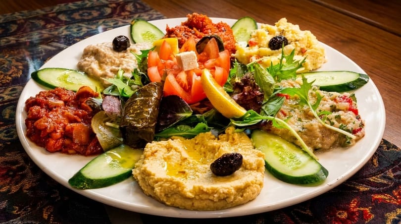 A vibrant mezze platter with hummus, baba ghanoush, stuffed grape leaves, and fresh vegetables.
